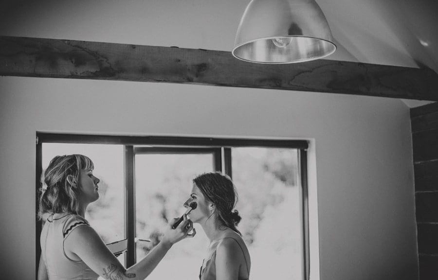 Makeup is applied to the brides face by the makeup artist next to a large window in the cottage
