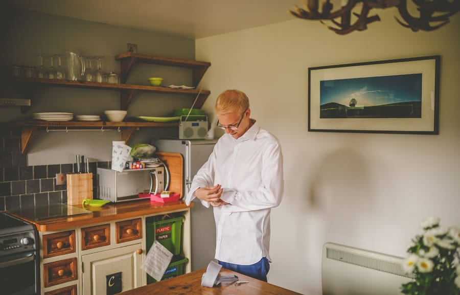 The groom puts on his cufflinks in the kitchen of the cottage