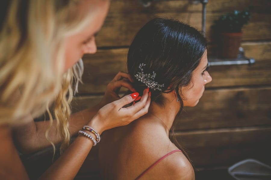 The hairdresser places a clip on the back of the brides hair as she sits down in the cottage