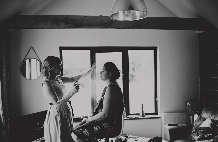 The makeup artist sprays a bridesmaid face as she sits down in the cottage