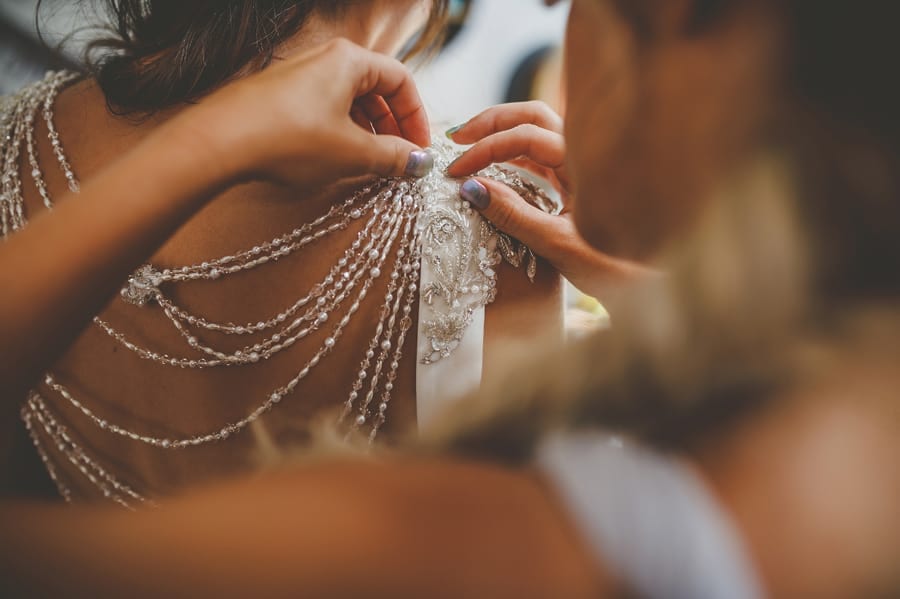 A bridesmaid fastens the back of the brides dress