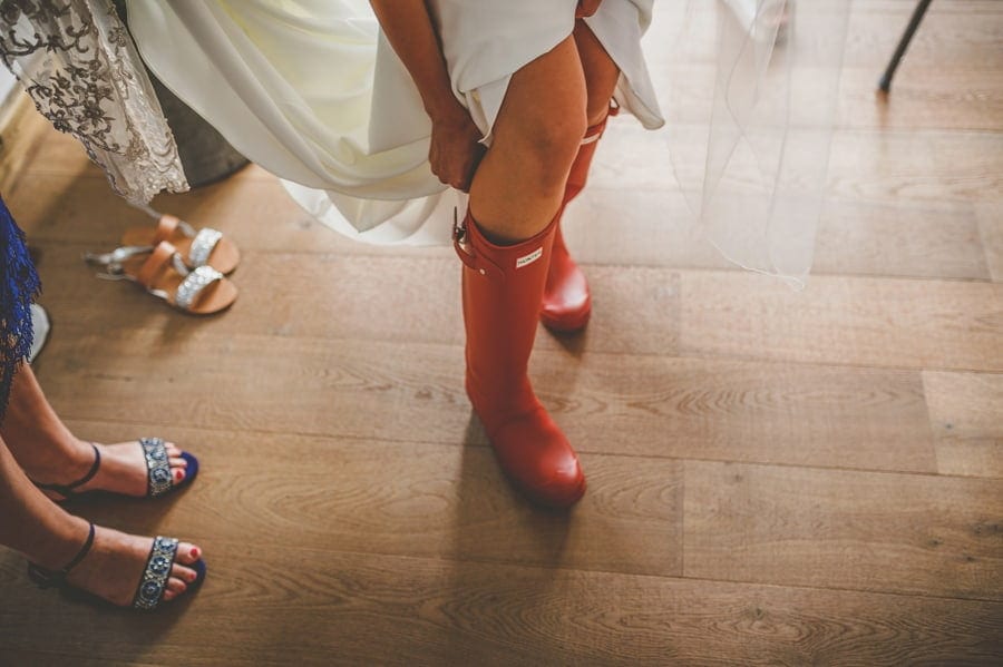The bride puts on her new red wellington boots in the kitchen of the cottage