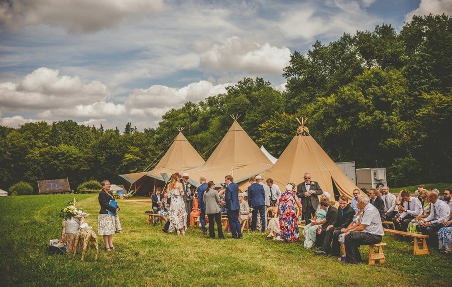 Wedding guests gather in the field next to the large tipi for the outdoor wedding ceremony at Yurt retreat in Crewkerne