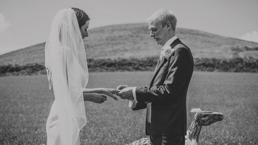The groom places a ring on the finger of the bride during the outdoor wedding ceremony