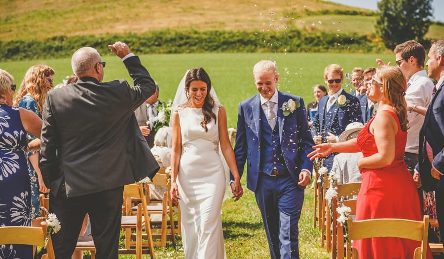 The bride and groom walk down the aisle of the outdoor ceremony as guests throw confetti in the air