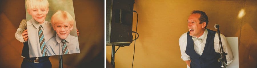 The grooms brother stands up and laughs at a board with a large photograph on it of the groom