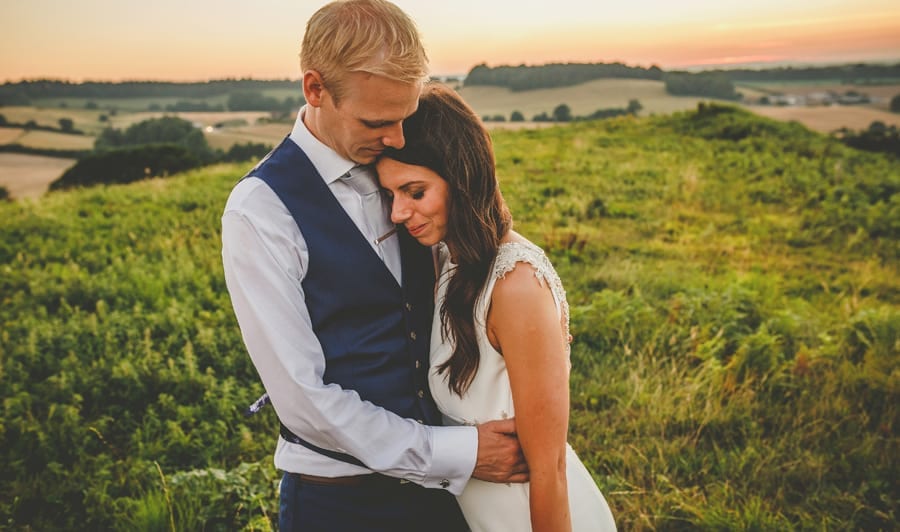 The bride puts her head on the grooms chest and closes her eyes on top of the hill at yurt retreat in Crewkerne, Somerset