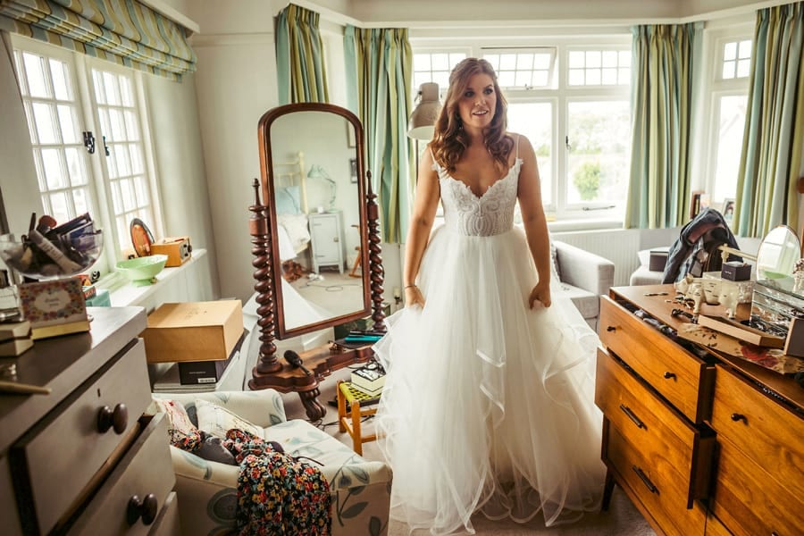 The bride stands in her parents bedroom with her wedding dress on