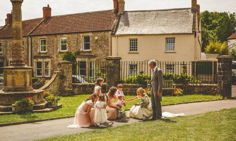 The bride and her father are greeted in the gardens of the Church by the flowergirls and bridesmaids