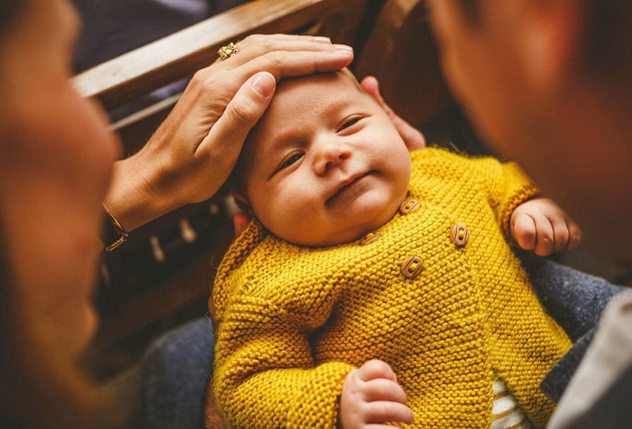 A lady puts her hand over the forehead of a baby boy as his mother holds him on her lap