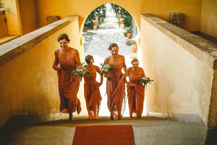 Bridesmaids walking up stone steps towards the wedding ceremony holding their bouquets