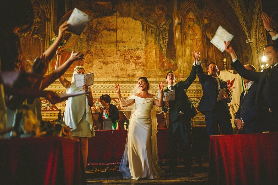 A bride and groom hold their hands up in the air and sing next to wedding guests during the wedding ceremony