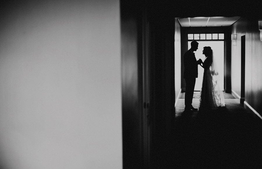 The bride and groom stand in a corridor and hold hands as they look each other