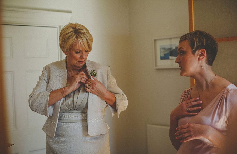 The brides mother places a flower onto the left side of her jacket