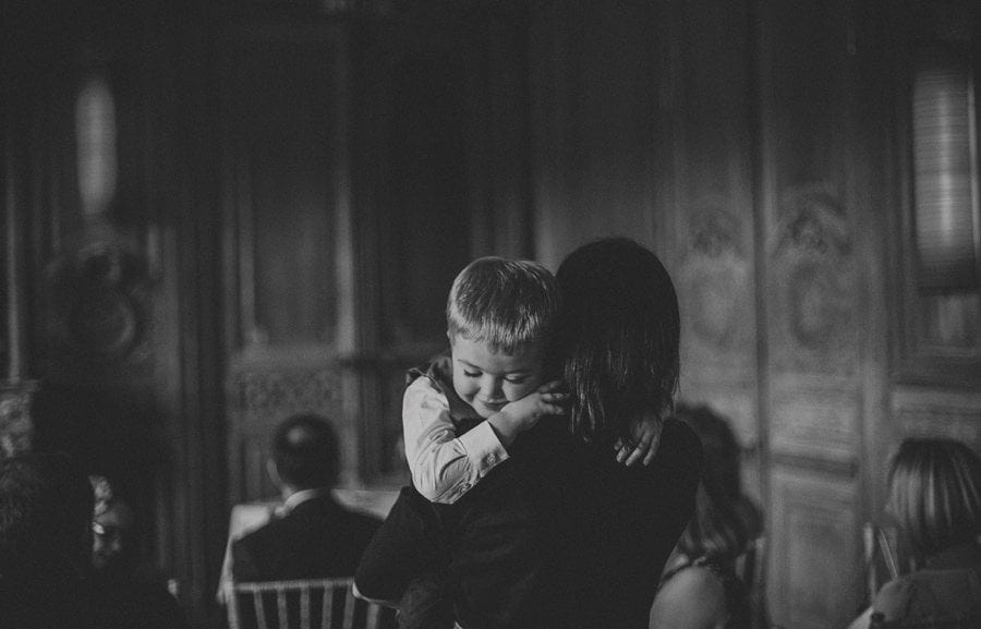A little boy closes his eyes and puts his head on his mothers shoulder as she carries him across a room at Cowley Manor