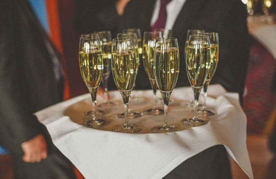 A tray of flutes filled with champagne is held by a waiter