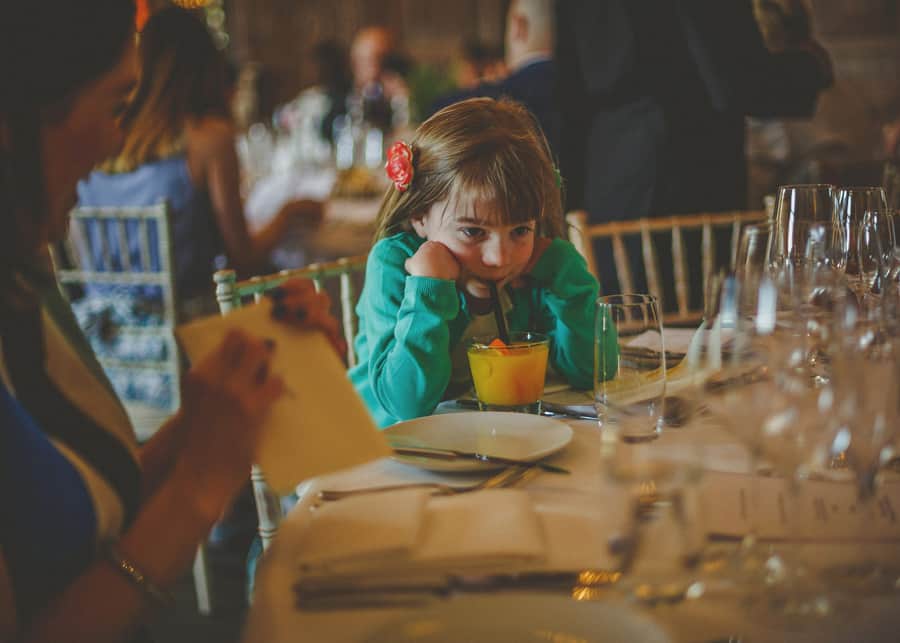 A little girl sits in a chair and sips a drink from a straw on the wedding table at Cowley Manor