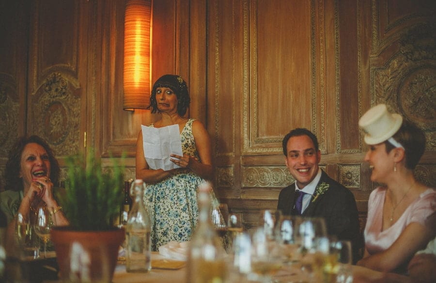 A bridesmaid stands in front of the wedding guests and delivers her speech as the groom smiles at the bride