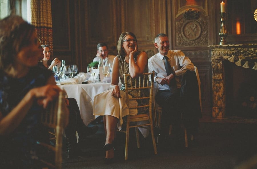 Wedding guests sat on chairs next to a table laugh at the speeches
