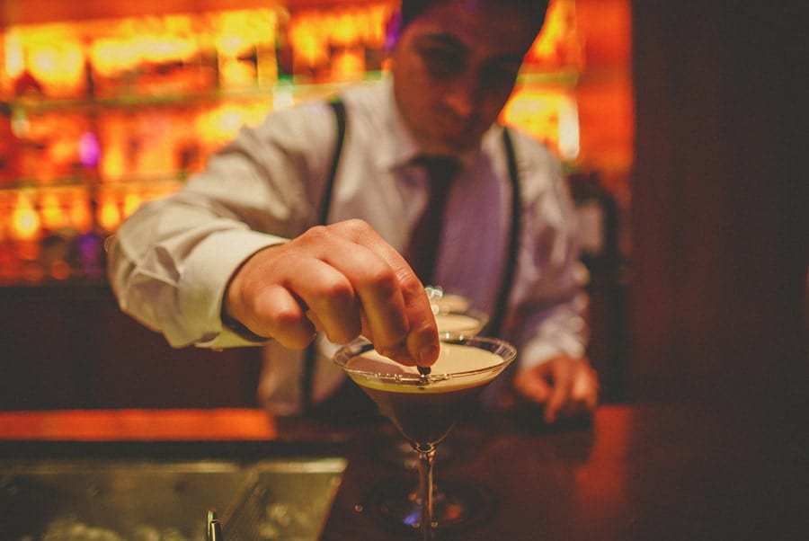 A bar man places a coffee bean into a cocktail drink on the bar