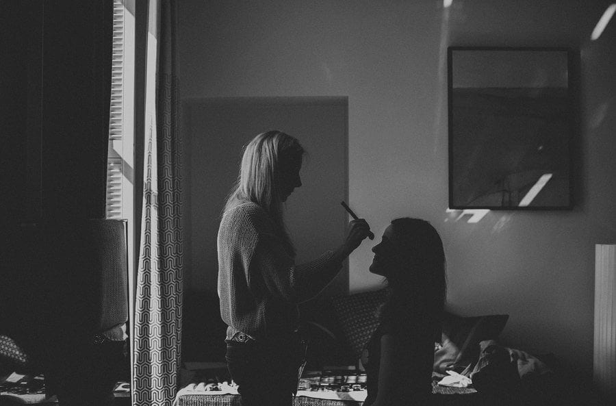 A makeup artist stands over a bridesmaid and brushes her nose with foundation