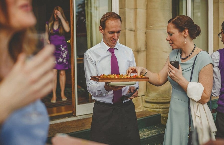 A wedding guest takes a canape from a tray held by a waiter in the gardens at Cowley Manor Hotel in Cheltenham