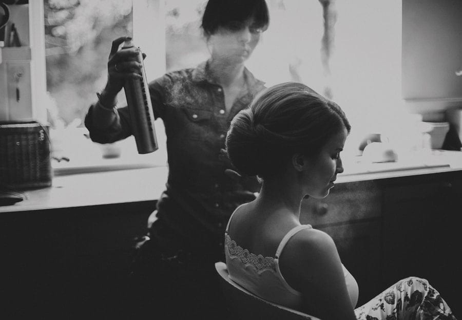 The make up artist sprays hair spray onto the brides hair