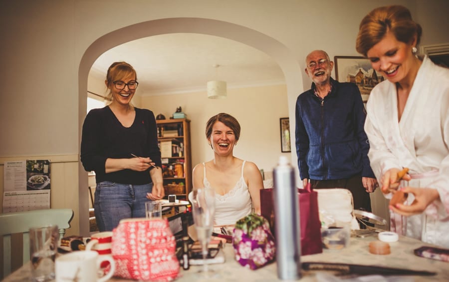 The bride laughs with her family in the kitchen of her parents house