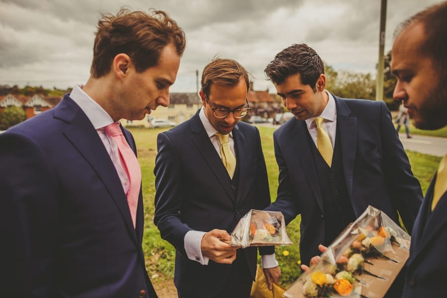 The groom and his ushers look at flowers fastened to a piece of cardboard