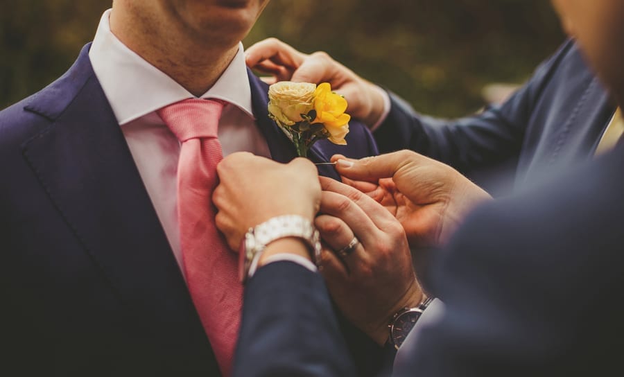 An usher places a pin through a flower as he fastens it to the grooms suit jacket