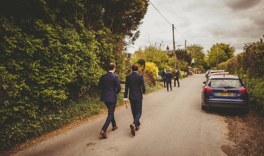 The groom and the ushers walk down a small road
