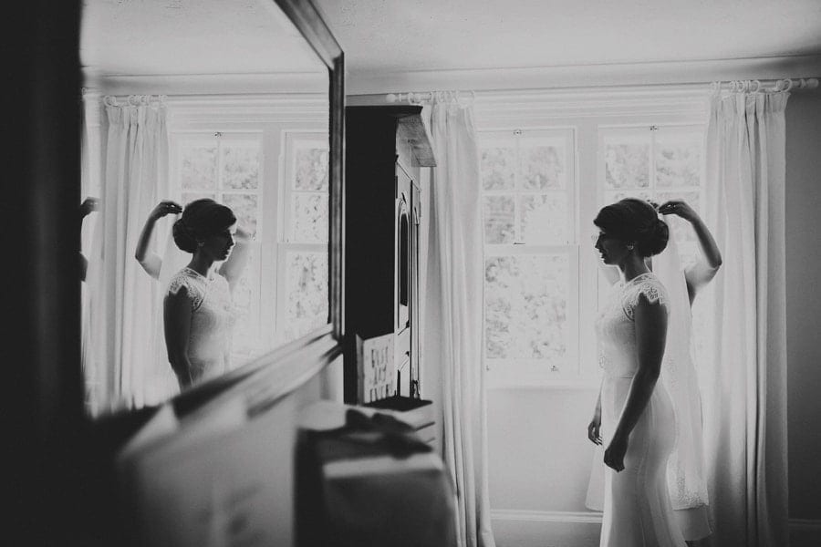 The bride looks in a mirror as her sister places her veil on the brides head