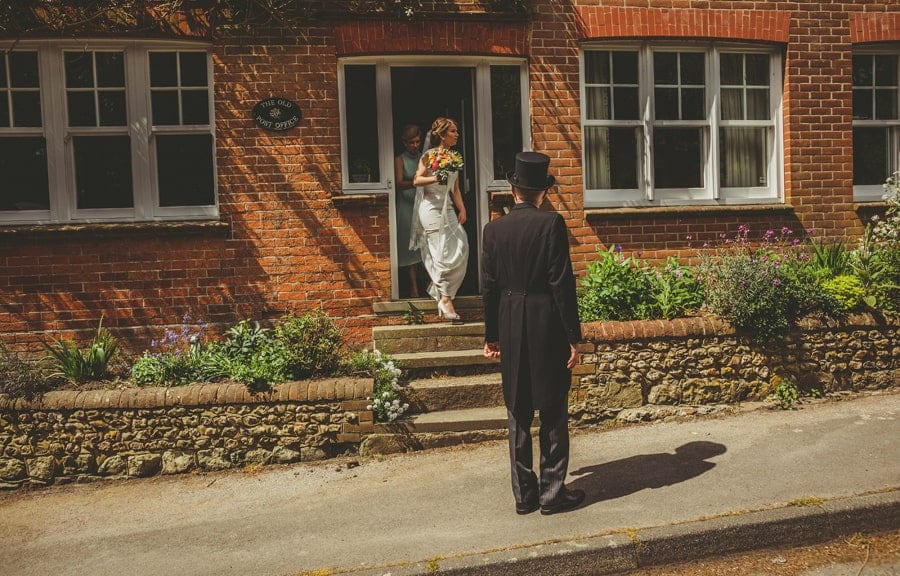 The brides father waits outside his house and the bride leave the house and walks down the steps