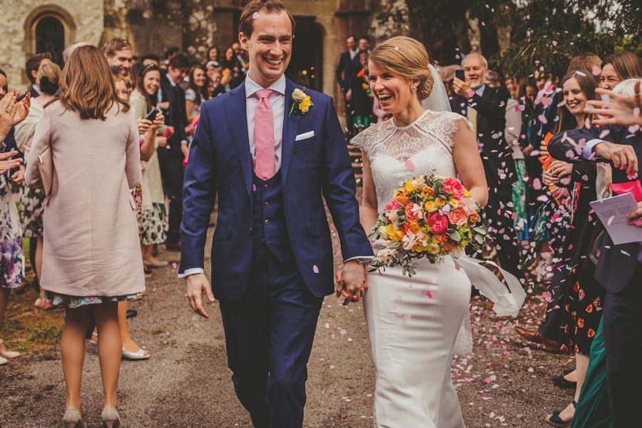 The bride and groom laugh with each other as confetti falls all around them outside the church