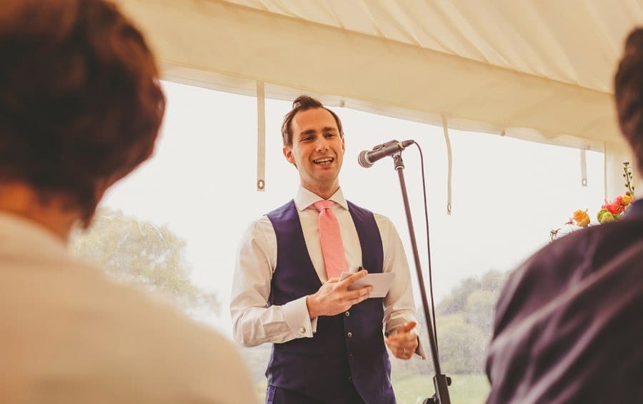 The groom stands in front of a microphone and delivers his speech in the marquee