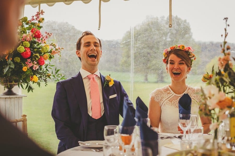 The bride and groom sit next to each other and laugh at the best mans wedding speech