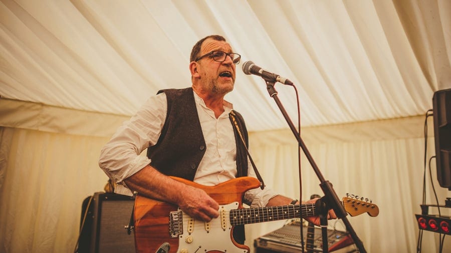 A member of the wedding band plays the guitar on stage in the marquee