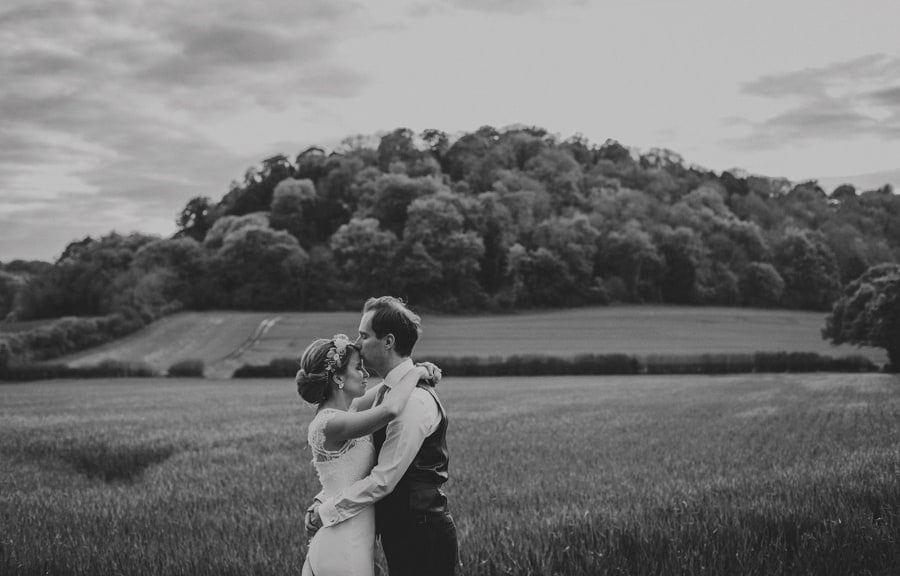 The groom kisses the bride on the forehead in a field