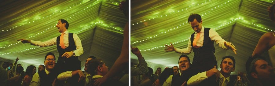 Wedding guests lift the groom onto their shoulders in the marquee