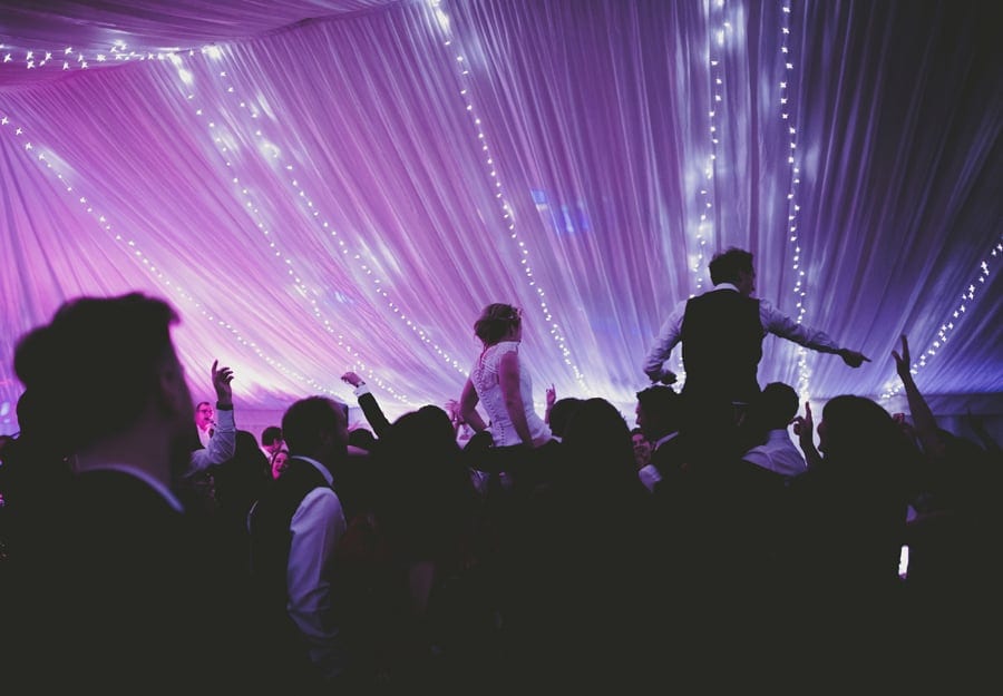 The bride and groom are lifted onto the wedding guests shoulders on the dancefloor of the marquee