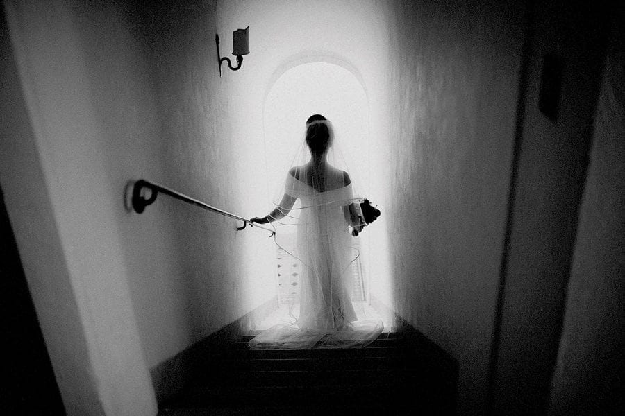 The bride walks down the stone steps holding onto the banister and holding her bouquet of flowers