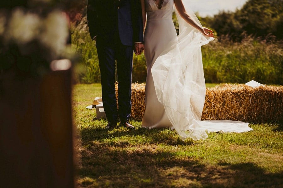 The bride moves her veil to one side as she stands next to the groom during the outdoor ceremony in a field