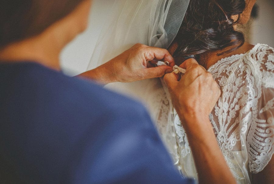 The mother of the bride fastens a button on the back of the brides dress
