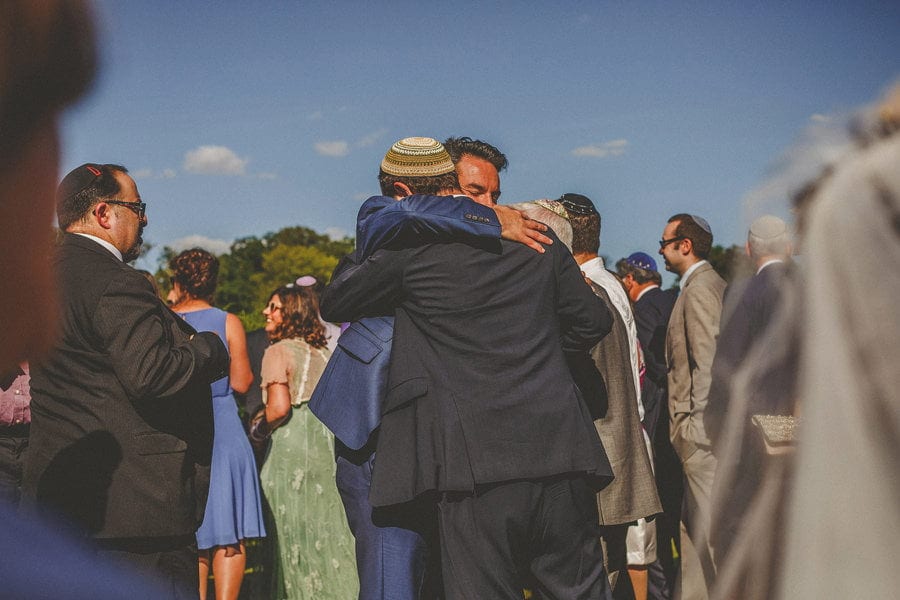 Wedding guests embrace the groom in the gardens at the outdoor wedding ceremony at Micklefield Hall