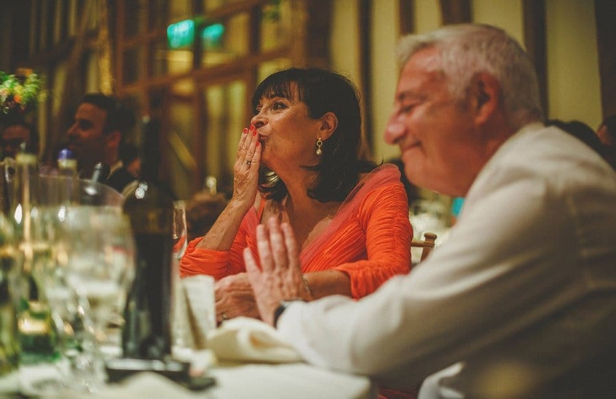 The groom's mother kisses her hand as she sits at the wedding table and listens to her sons wedding speech