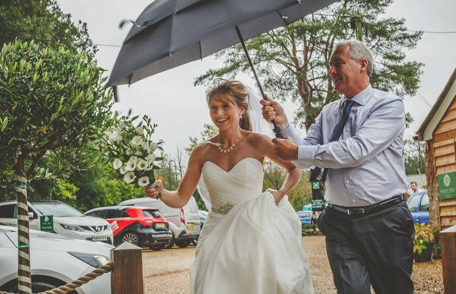 The bride arrives at Sopley Mill and a man holds an umbrella above her head