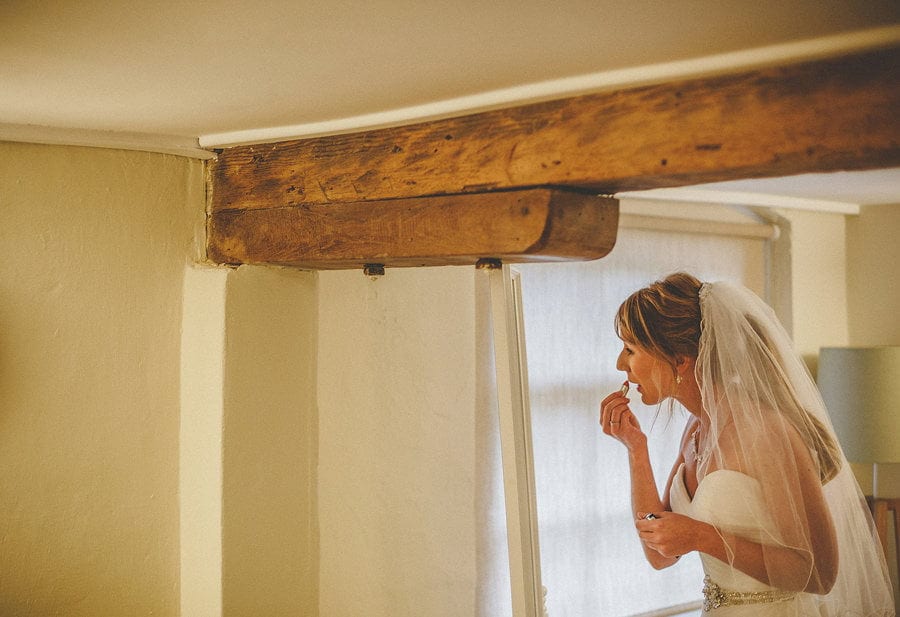 The bride looks into a mirror and applies lipstick to her lips at Sopley Mill