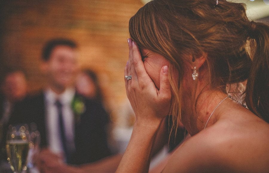 The bride puts her hands against her face and laughs