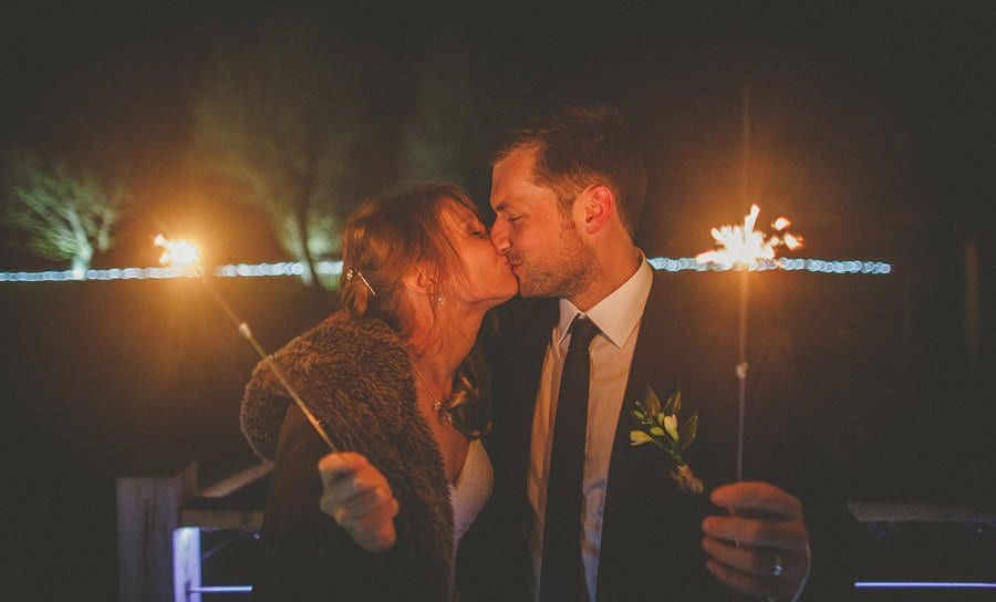 The bride and groom kiss each other and hold sparklers outside Sopley Mill