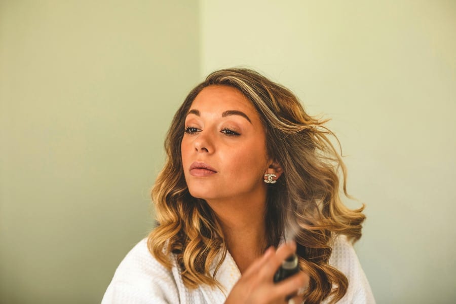 The bride sprays hairspray onto her hair